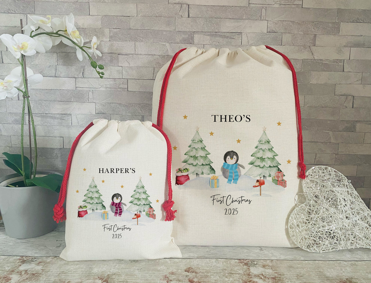 Personalised Christmas gift sacks with penguin and tree design both with red drawstrings and 'First Christmas 2025' printed below