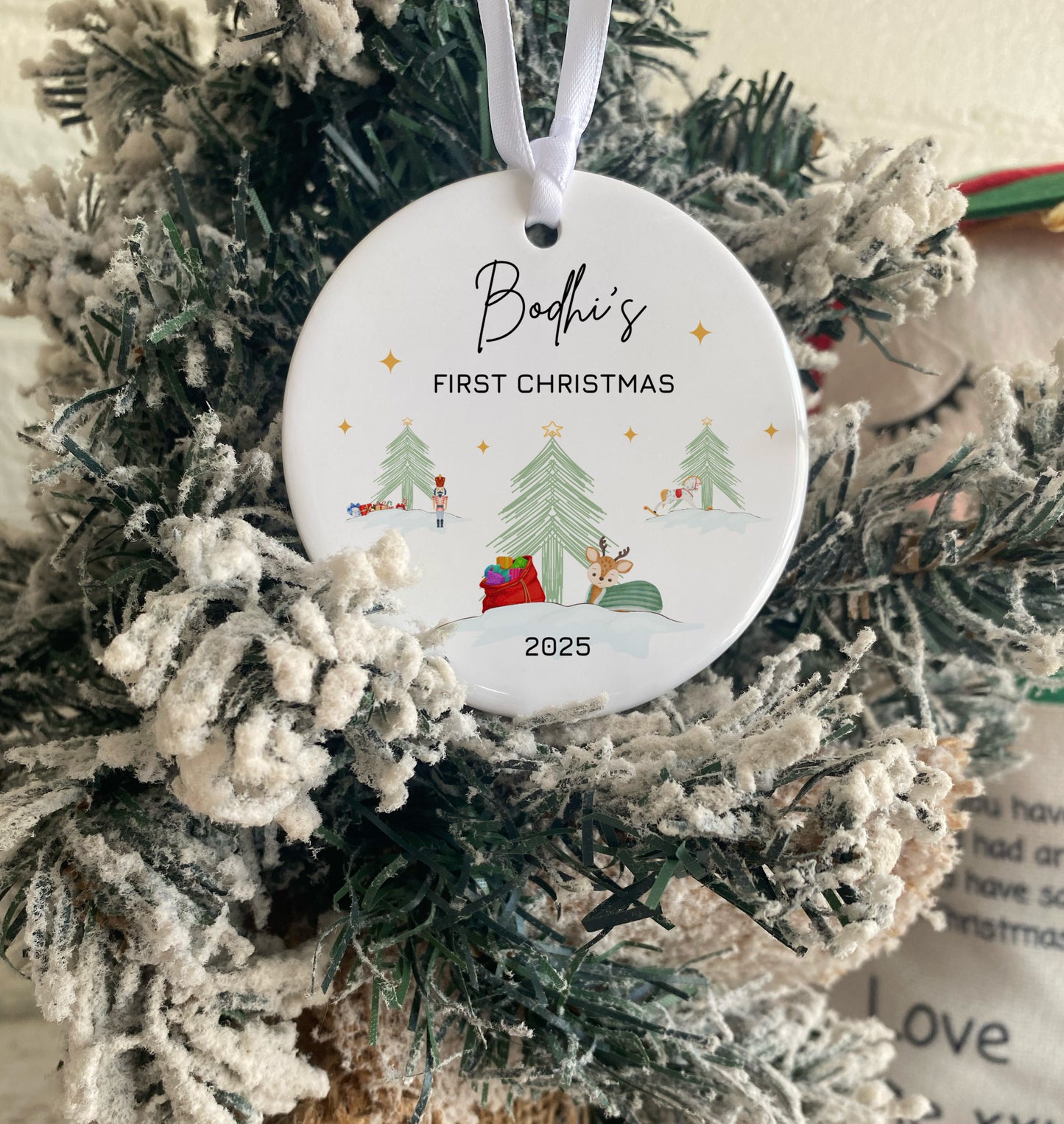 Christmas ornament with 'Bodhi's First Christmas 2025' text on a decorated tree.