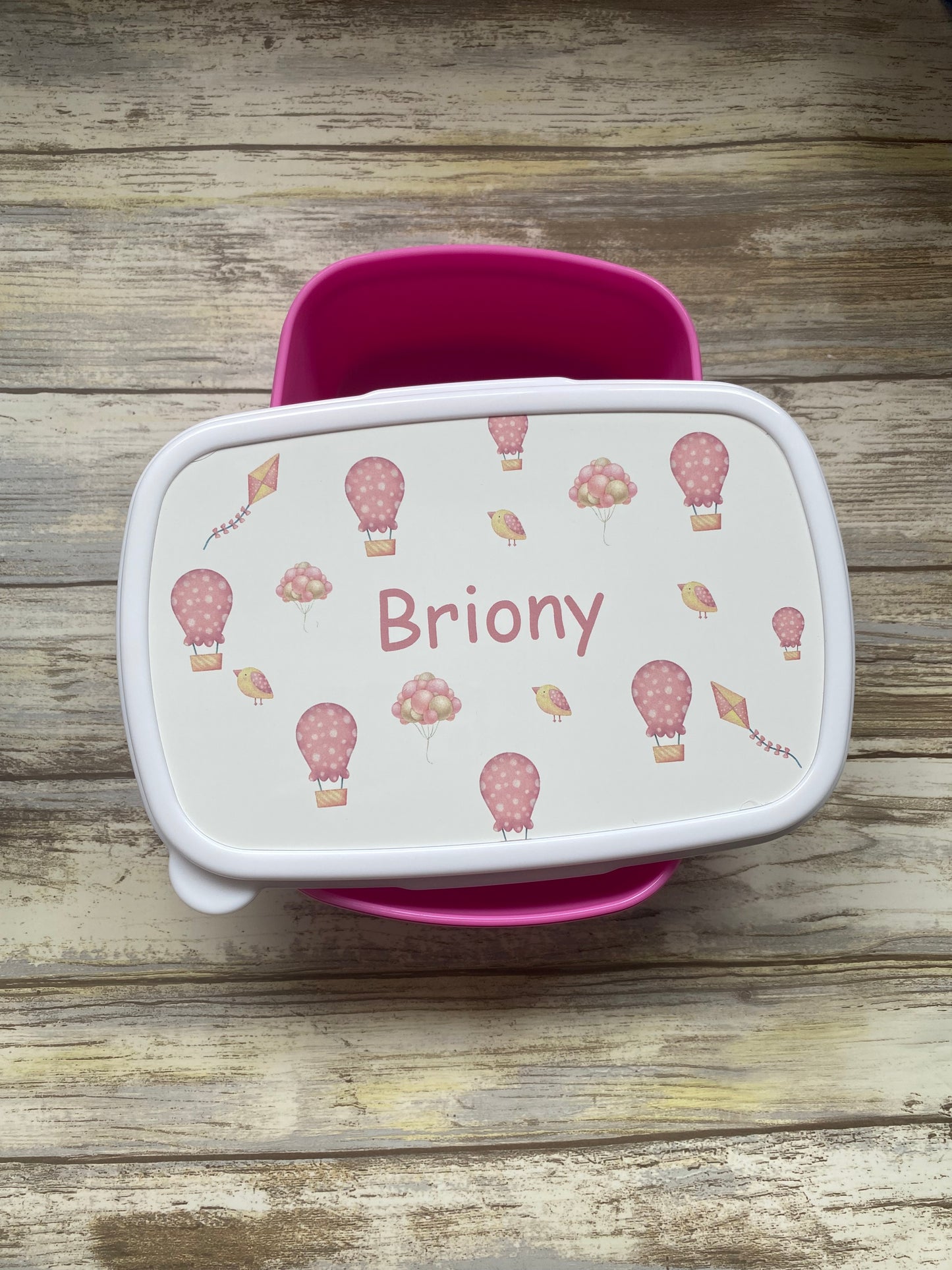 Personalised pink lunch box for a girl named Briony, featuring a cute design with hot air balloons, kites, and small birds — a unique gift for school or nursery.