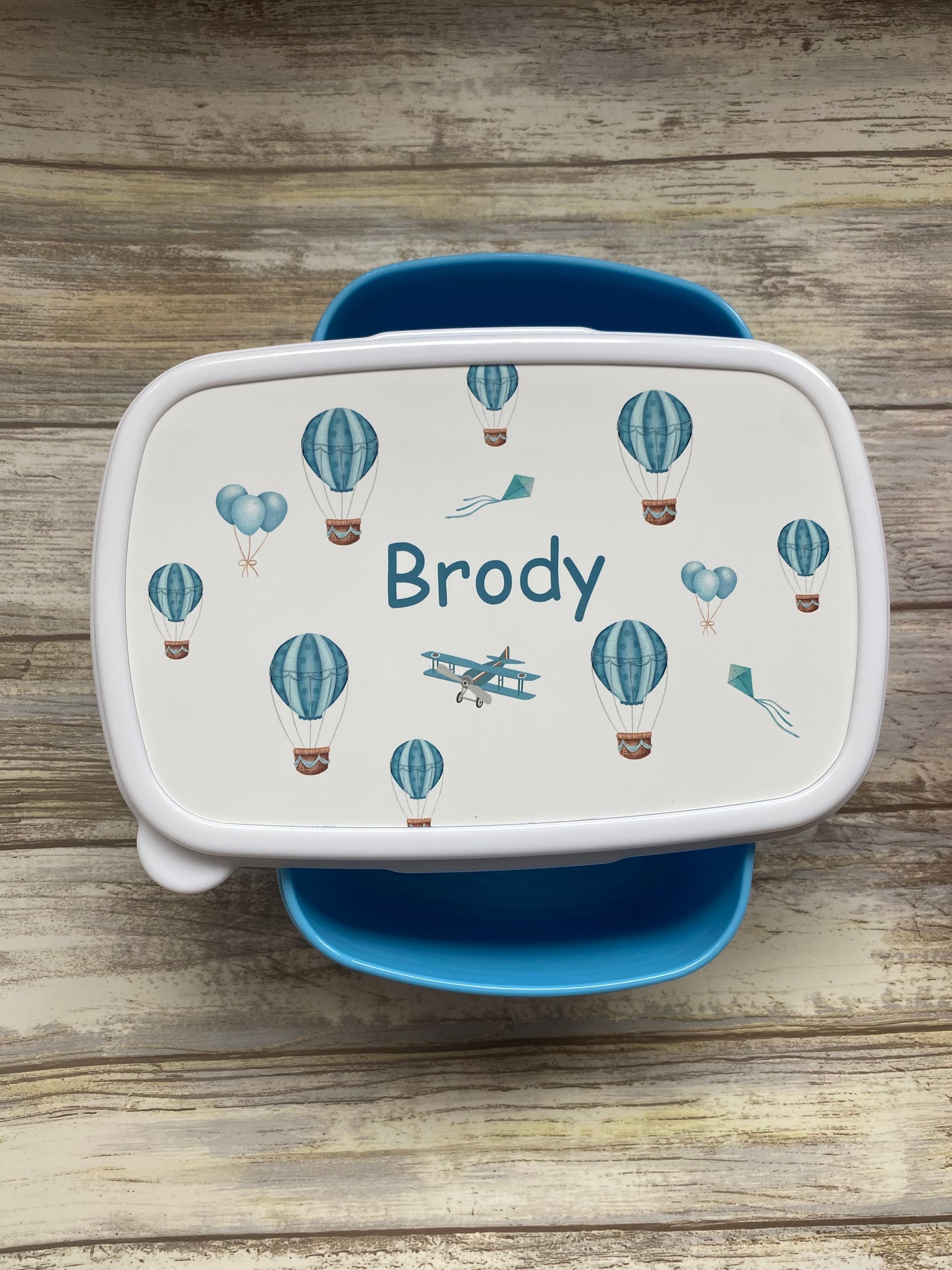 Personalised blue lunch box for a boy named Brody, adorned with hot air balloon, airplane, and kite illustrations — a unique, custom gift ideal for school or nursery.