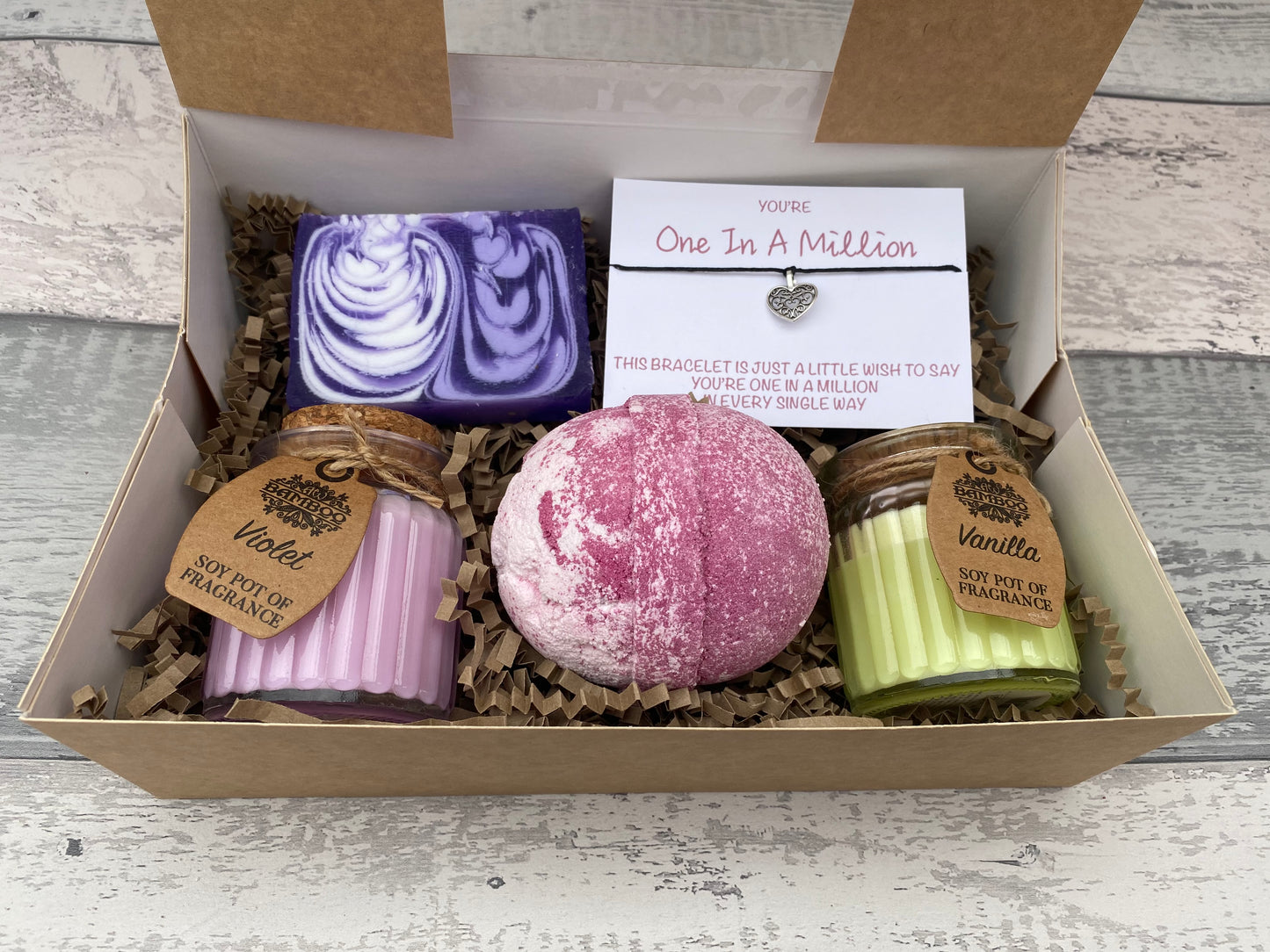 Gift set with bath bombs, candles, and a bracelet in a box on a wooden surface