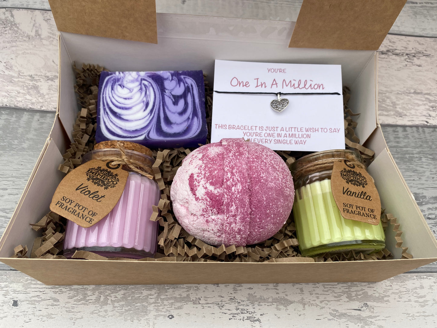 Gift set with bath bombs, candles, and a card in a box on a wooden surface
