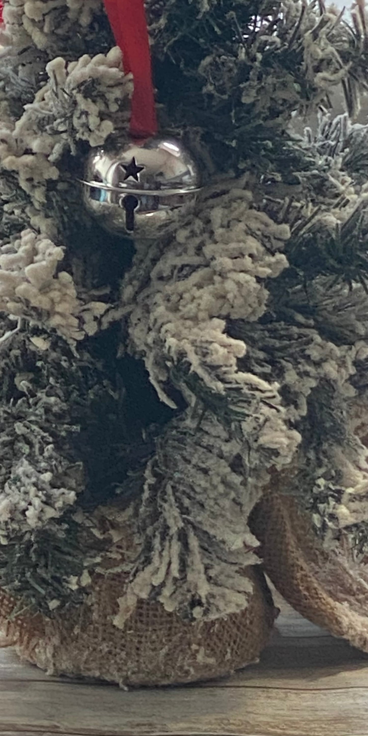 Close-up of a Christmas tree ornament with a bell and star on a wooden surface.