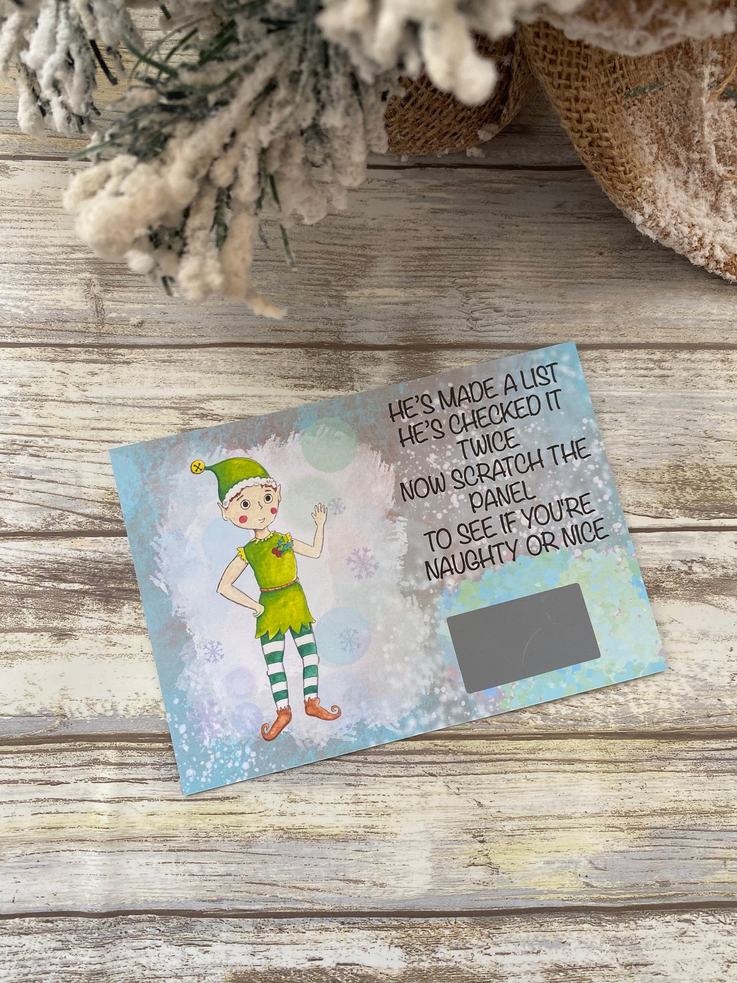 Christmas-themed scratch-off card with an elf illustration on a wooden surface.