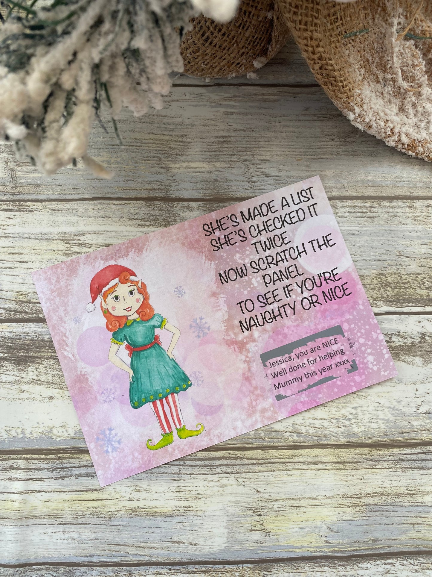Scratch card with a Girl elf in a green dress and red hat on a wooden surface.