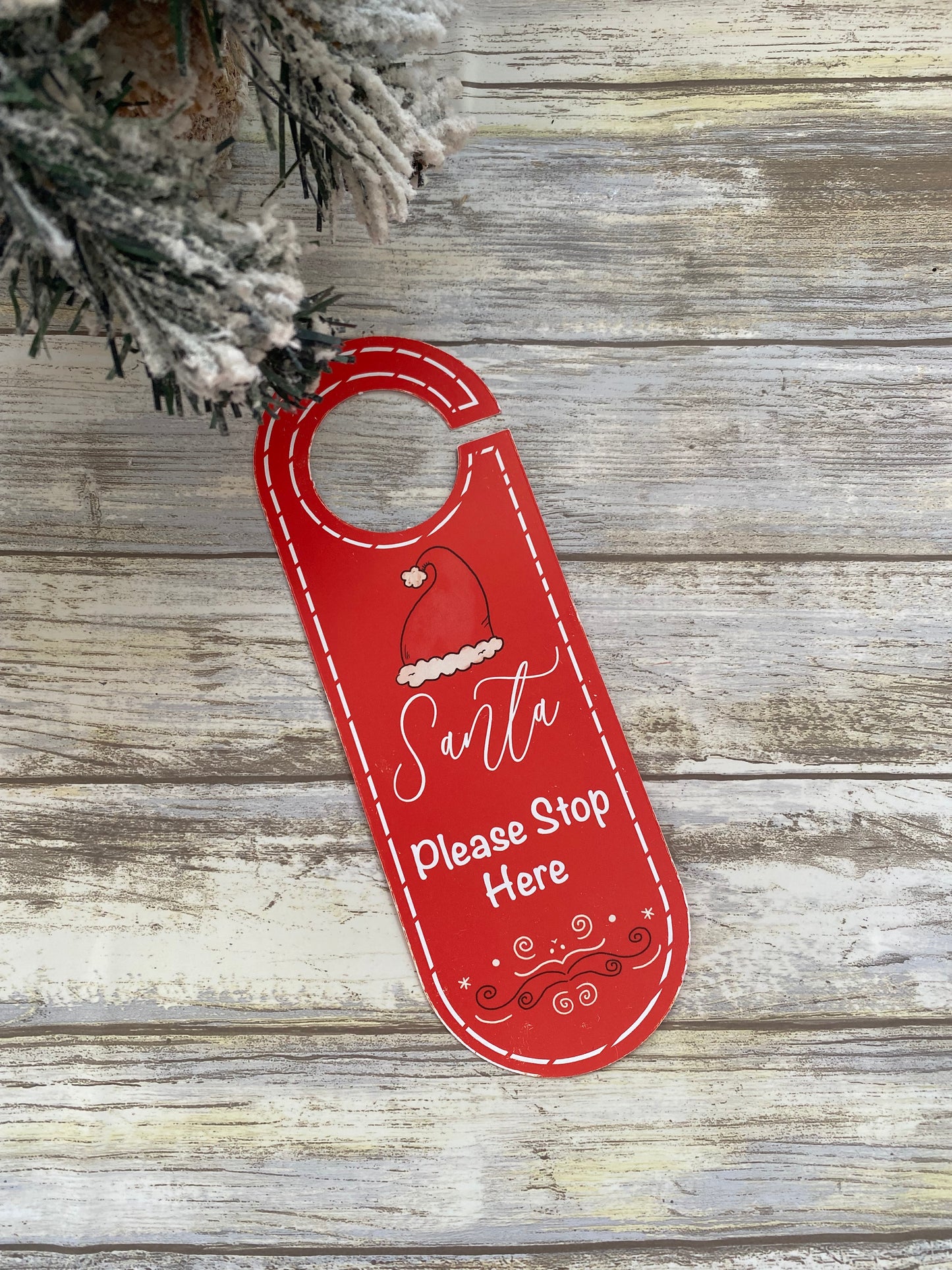 Red door sign with 'Santa Please Stop Here' text on a wooden background