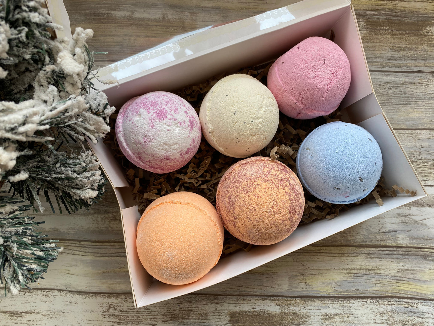 Box of six colorful bath bombs on a wooden surface with decorative elements.