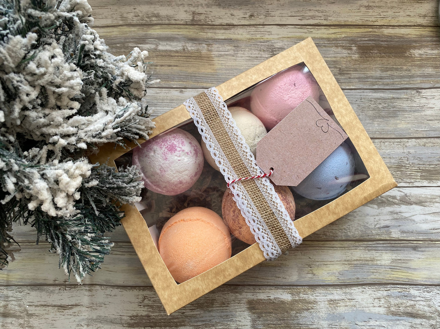 Box of bath bombs with a decorative tag on a wooden surface next to a small Christmas tree.