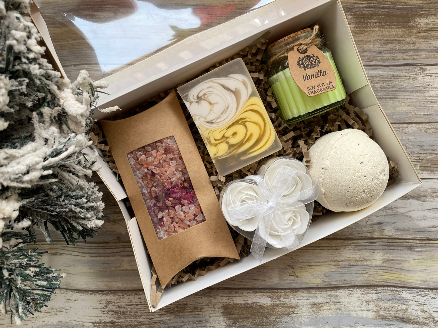 Gift box with bath products including a bath bomb, soap, and bath salts on a wooden surface.
