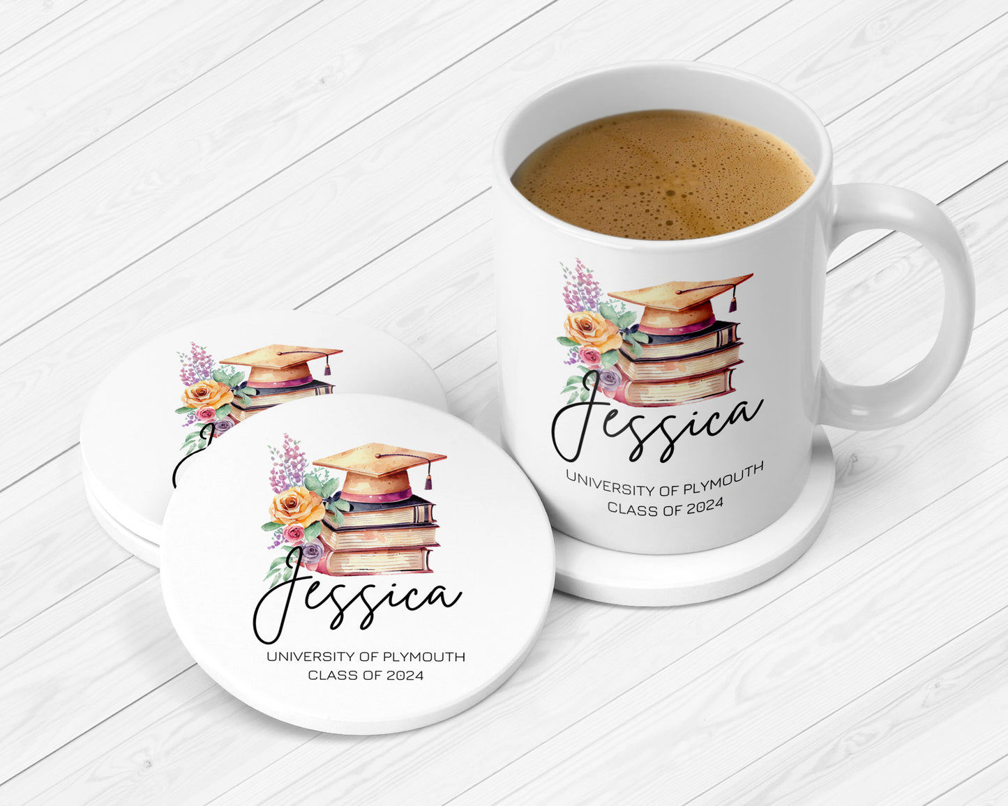 A white ceramic mug and matching coasters featuring a personalized graduation design. The artwork includes a watercolor-style stack of books topped with a gold graduation cap, accented by yellow and purple flowers. Below the illustration is the name “Jessica” in elegant script, followed by the text “University of Plymouth, Class of 2024” in uppercase letters. The set is placed on a white wooden surface, and the mug is filled with frothy coffee.