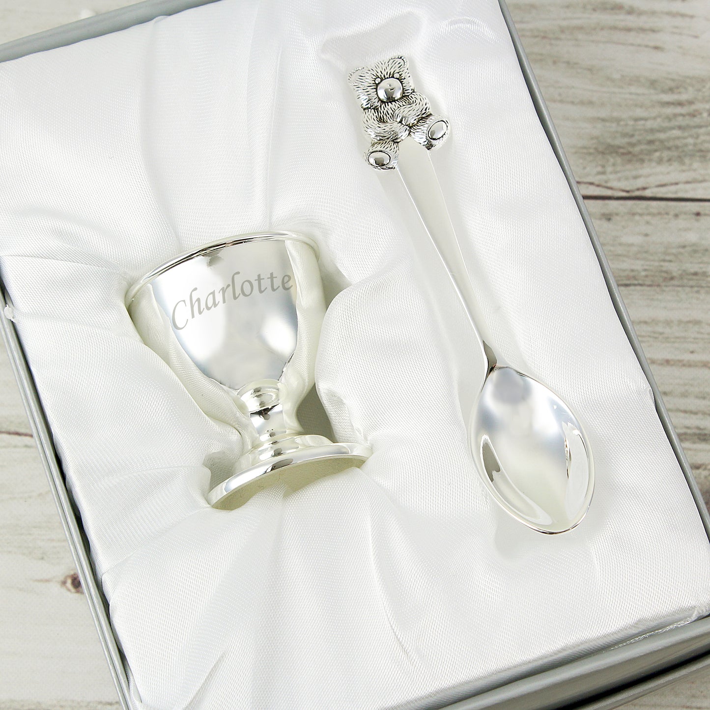 Silver baby cup and spoon set with 'Charlotte' engraving in a box on a wooden surface