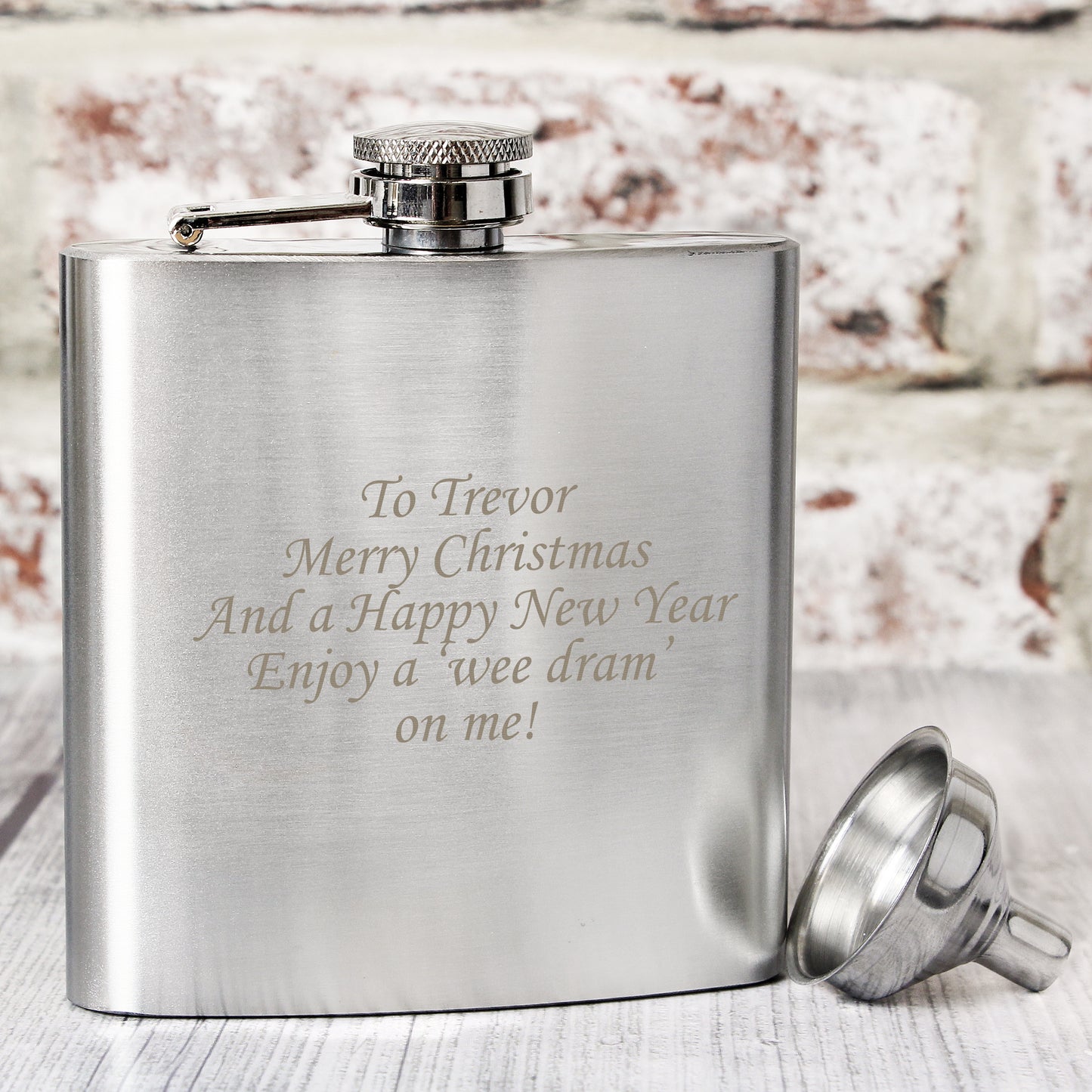 Silver hip flask with engraved text on a wooden surface