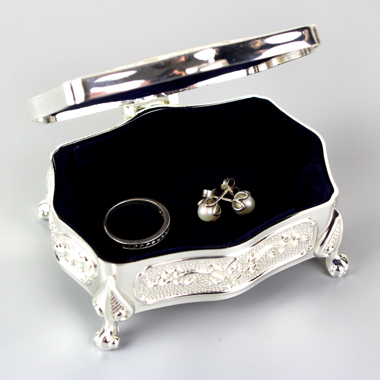 Silver jewelry box with a black interior containing a ring and earrings on a light gray background