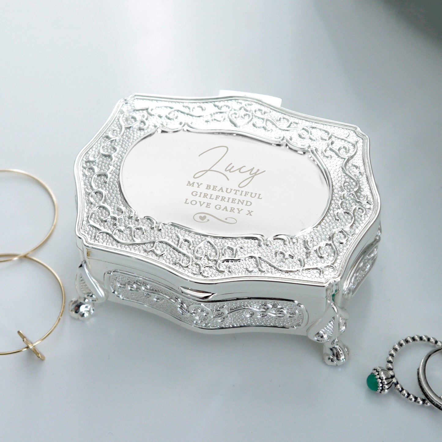 Decorative silver jewellery box with engraved text on a light grey background