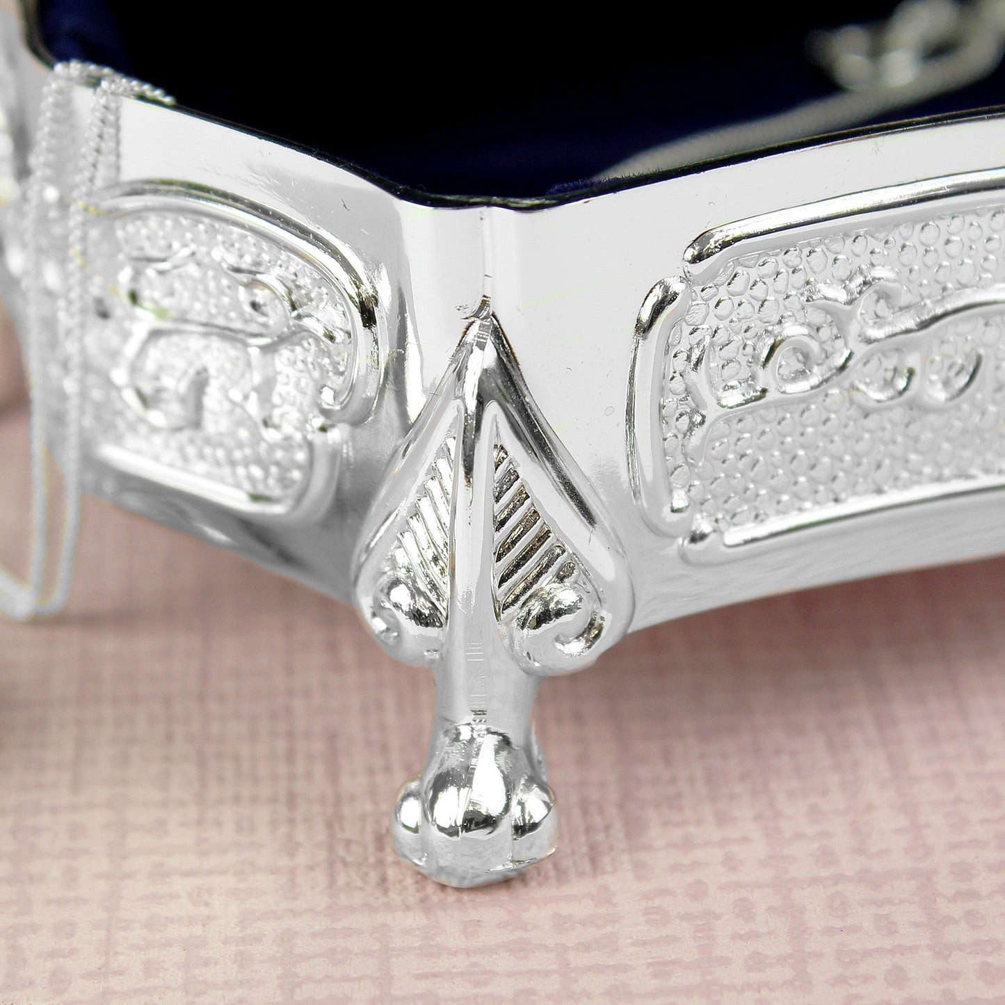 Close-up of a silver box with intricate designs on a pink fabric background