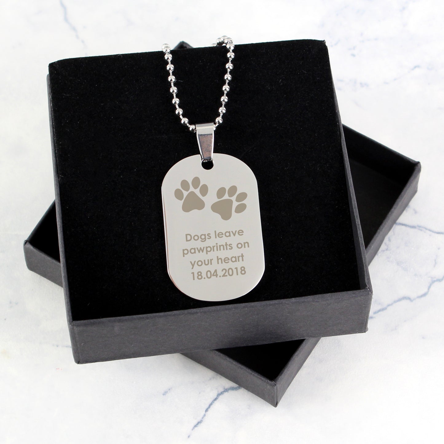 Silver dog tag necklace with engraved message on a black box