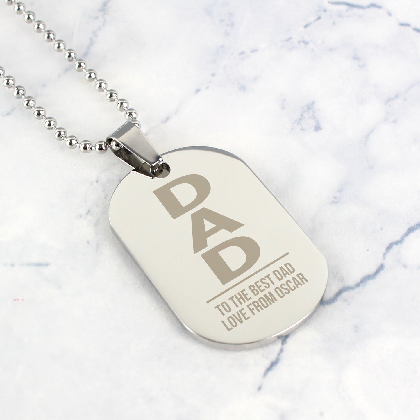 Dog tag necklace with 'DAD' engraving on a marble background