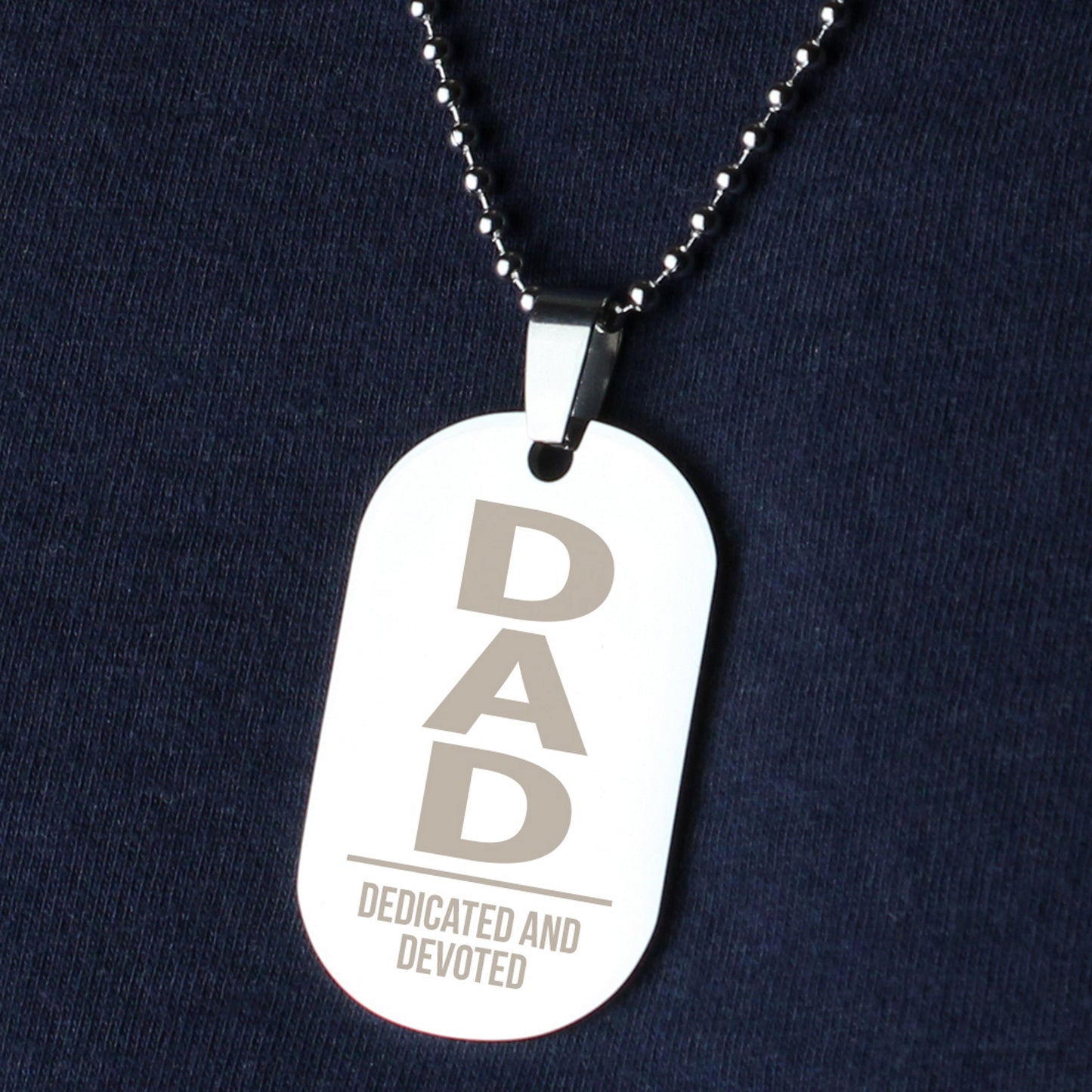 Dog tag necklace with 'DAD Dedicated and Devoted' text on a dark blue background