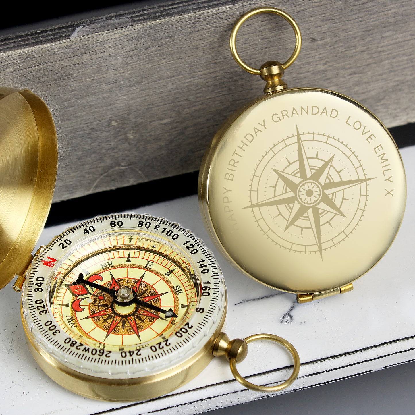 Gold pocket compass with engraved text on a wooden surface