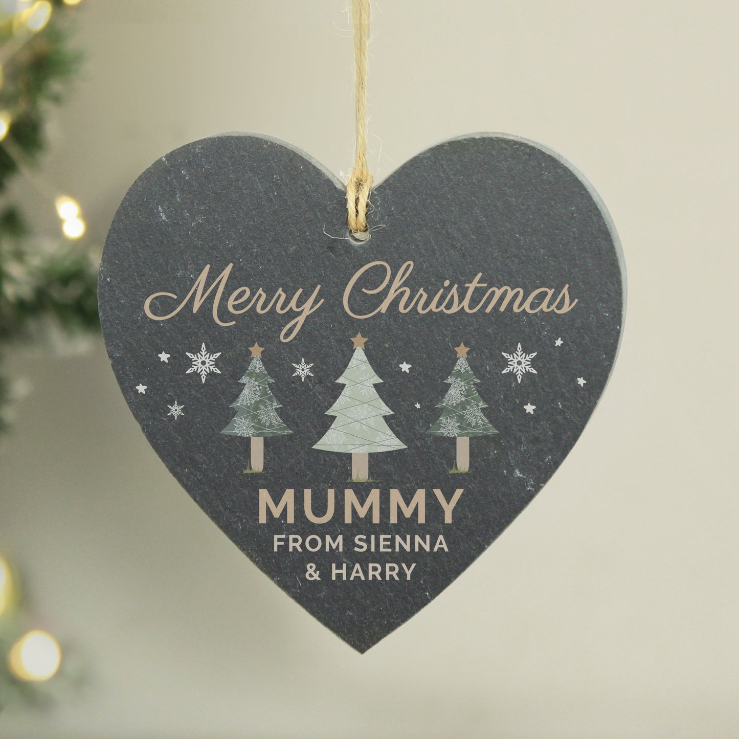 Heart-shaped Christmas ornament with 'Merry Christmas Mummy' text and tree illustrations, hanging against a neutral background.