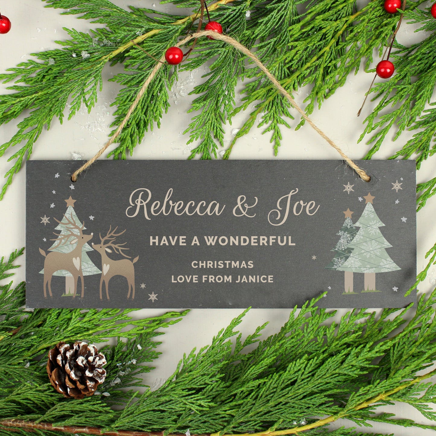 Personalised Christmas sign with reindeer and trees on a background of greenery and berries.