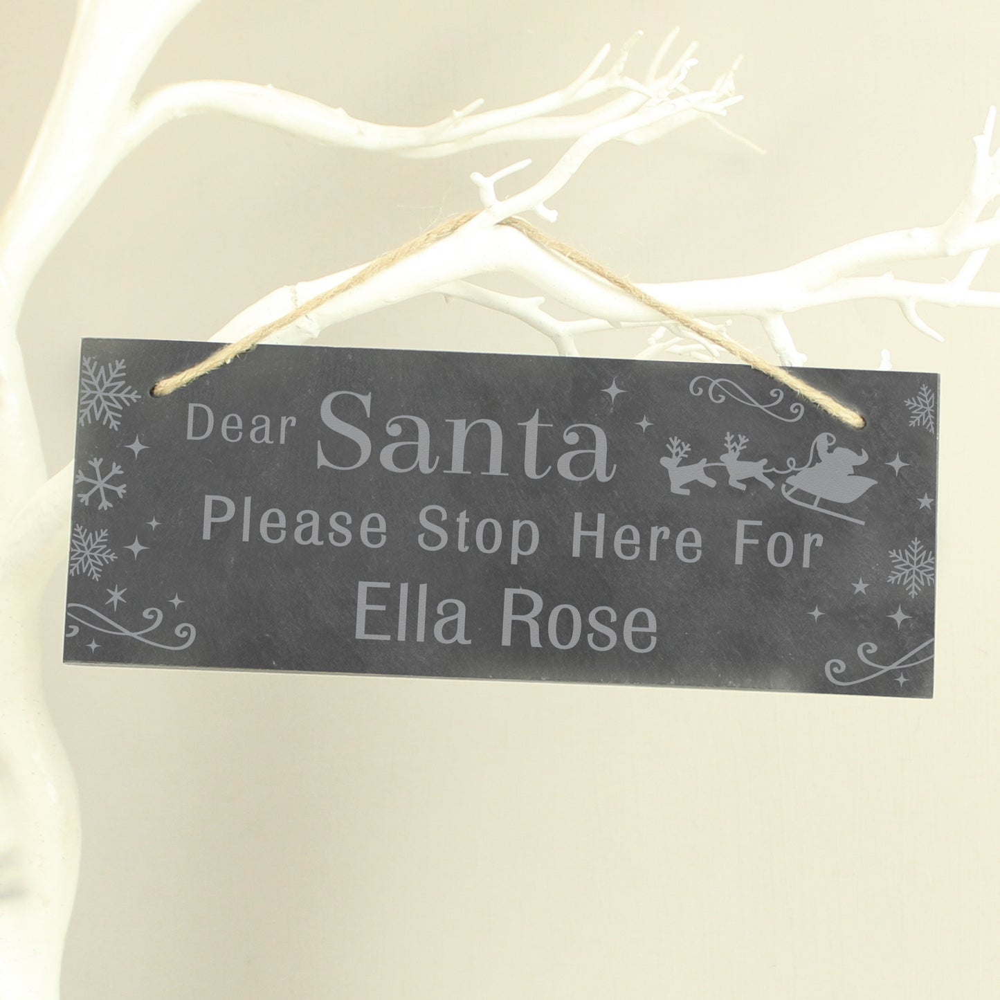 Decorative sign for Christmas with text 'Dear Santa Please Stop Here For Ella Rose' on a branch.