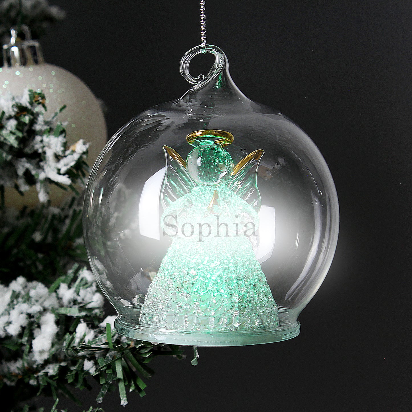 Decorative angel ornament with 'Sophia' inside a glass bubble, Christmas tree in the background