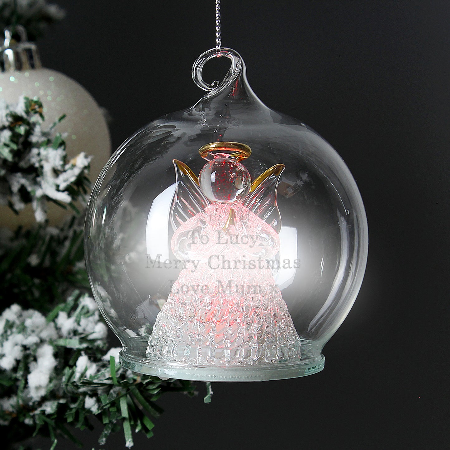 Decorative angel ornament in a glass bubble with text, Christmas tree in the background