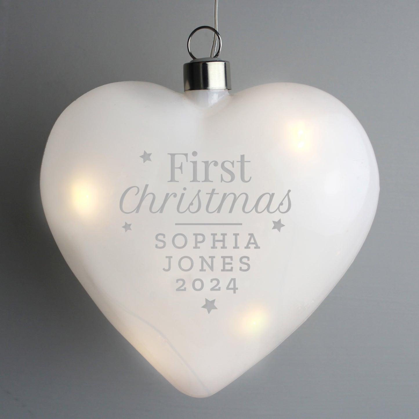 Heart-shaped ornament with 'First Christmas' engraving on a gray background