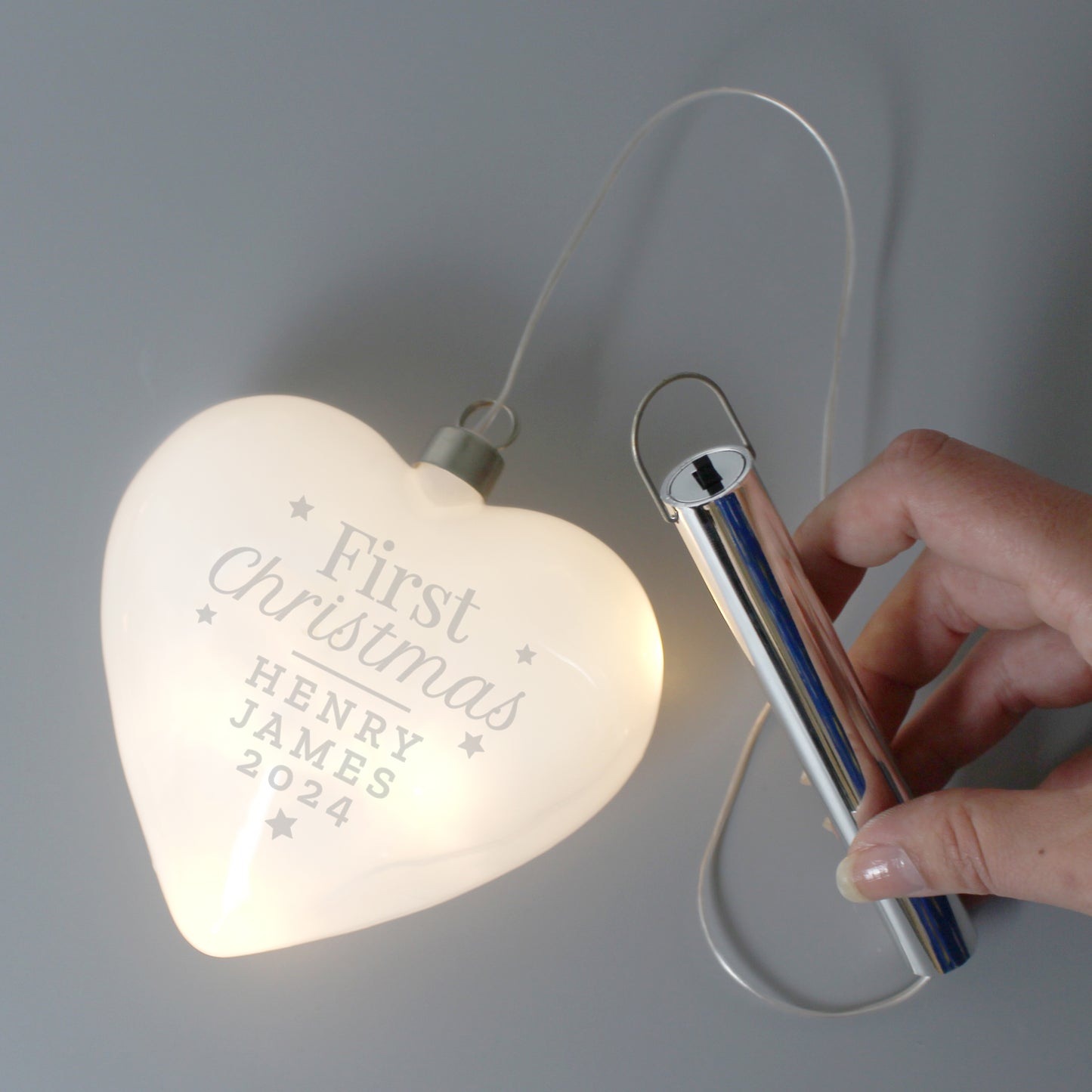Heart-shaped light with engraved text and a hand holding a carabiner against a gray background