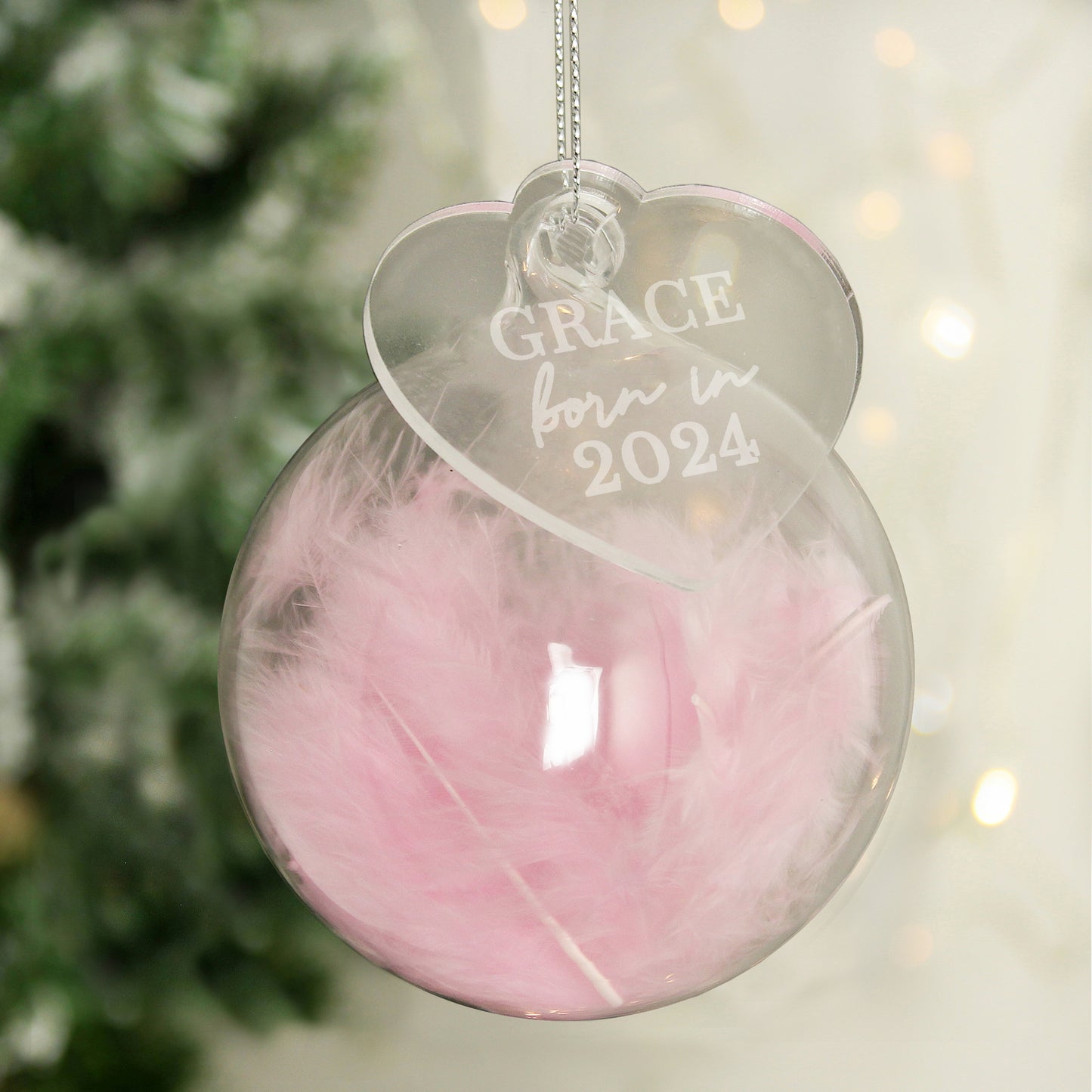 Decorative ornament with 'GRACE born in 2024' text, hanging against a blurred Christmas tree background.