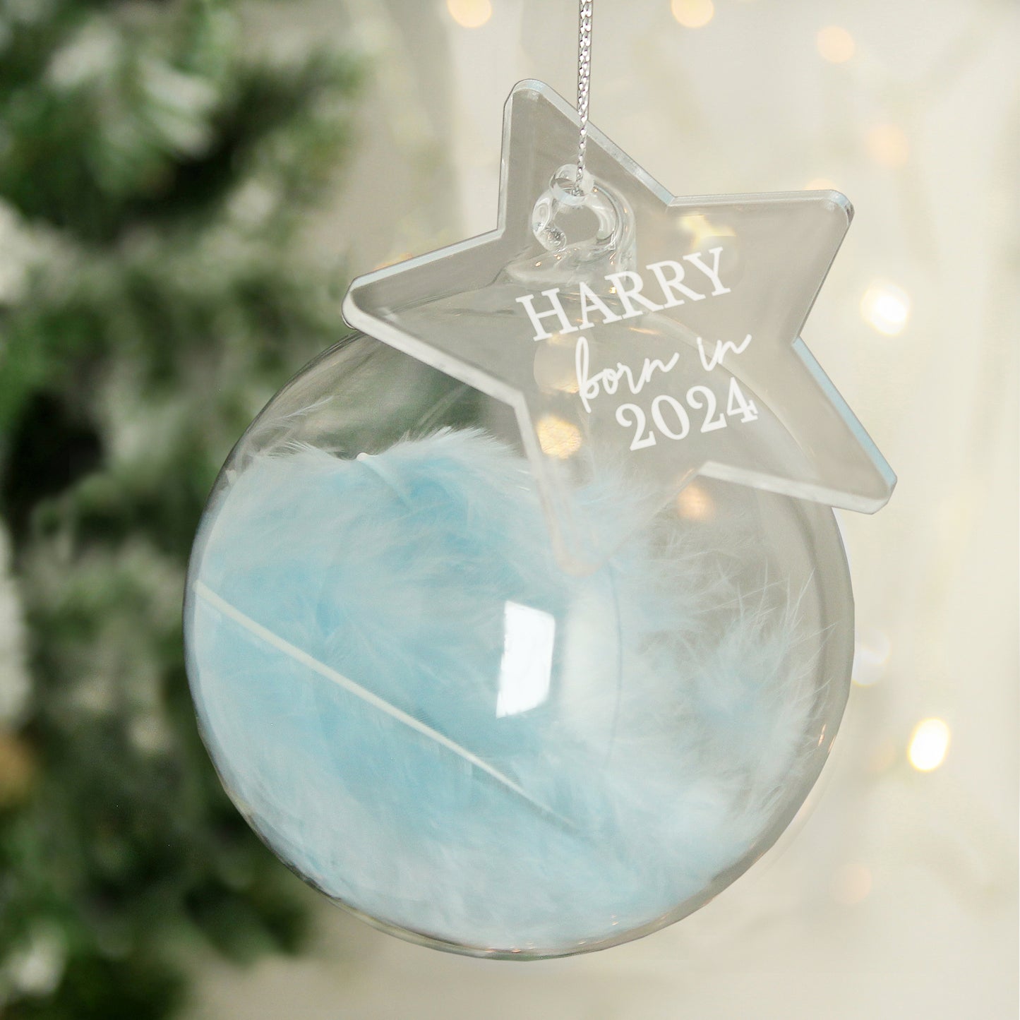Personalised Decorative ornament with a star-shaped tag reading 'Harry born in 2024' against a blurred Christmas tree background.