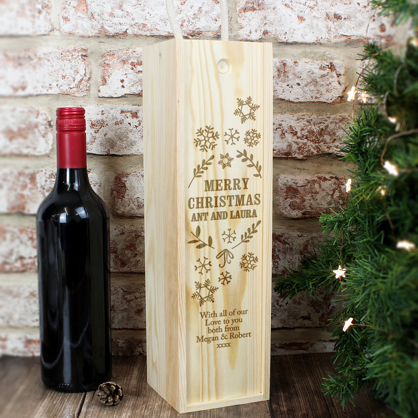 Wooden wine box with engraved text next to a bottle of red wine against a brick wall.