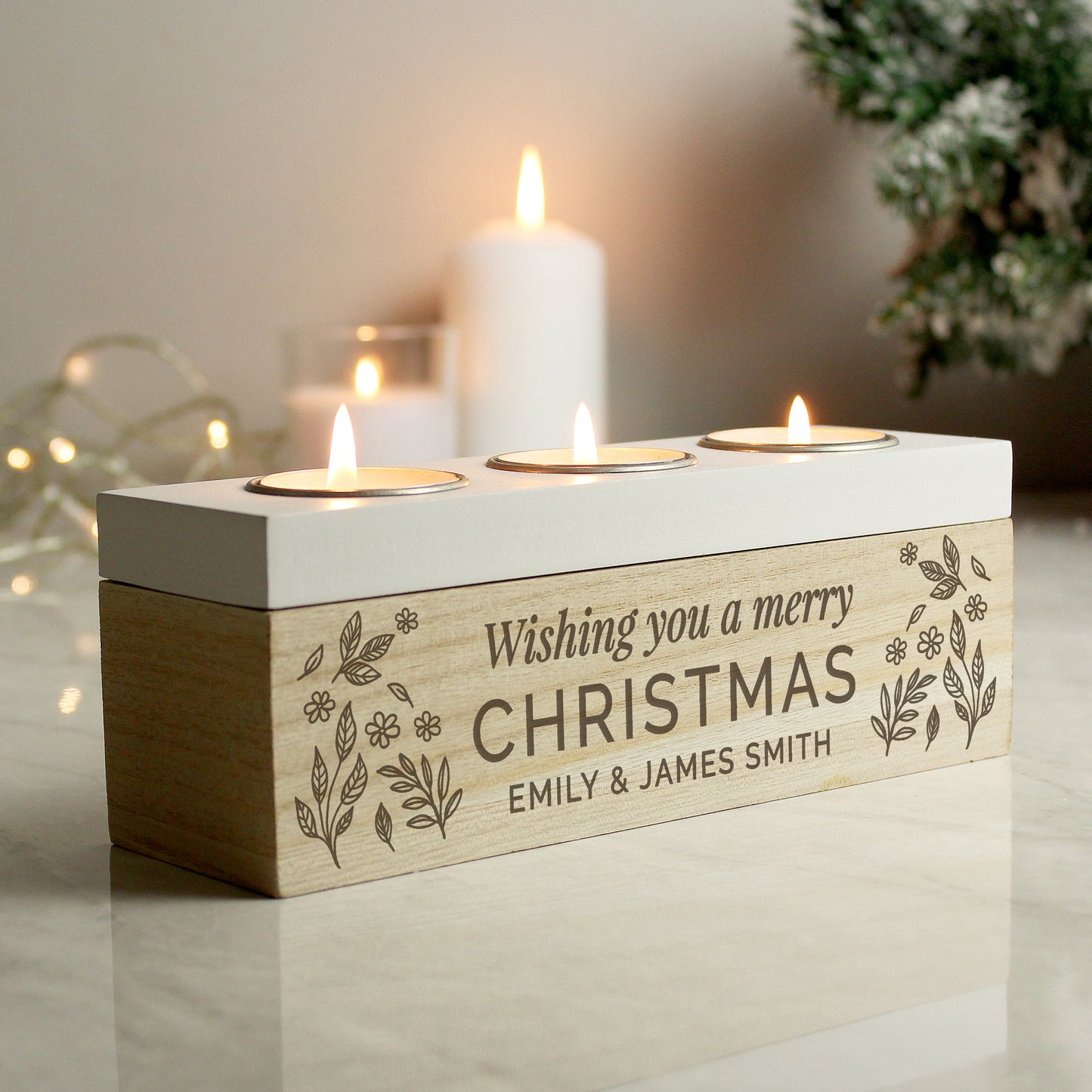 Wooden candle holder with 'Wishing you a merry Christmas' text and three lit candles on a reflective surface.