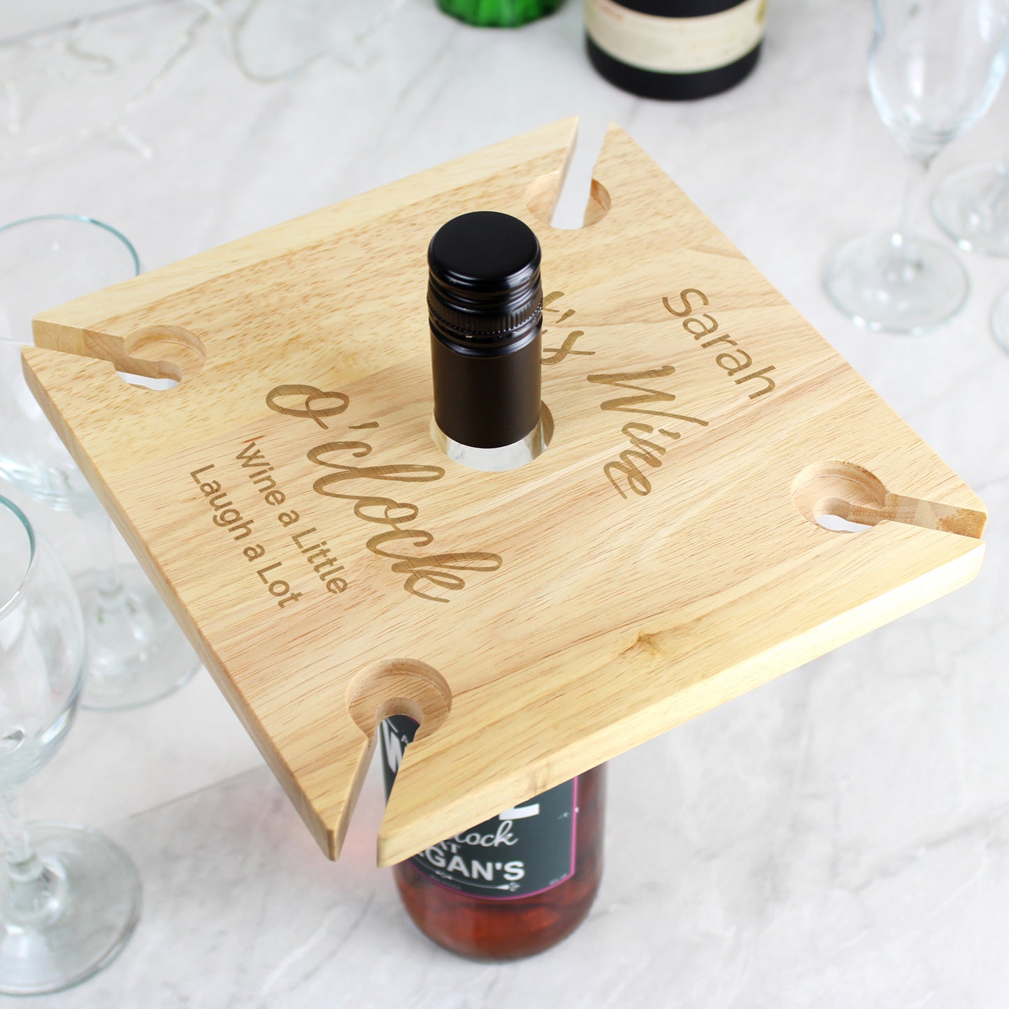 Wooden bottle holder with engraved text on a white surface with wine bottles and glasses.