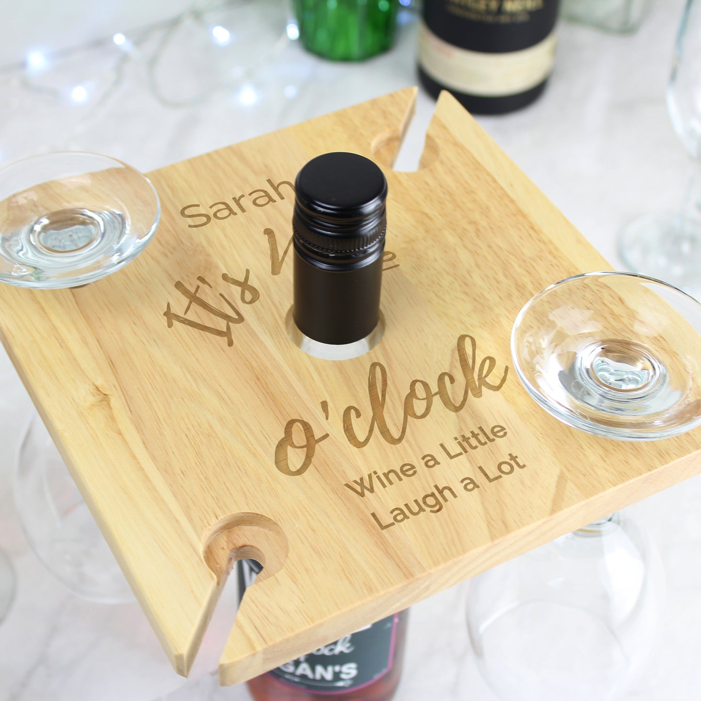 Wooden wine holder with engraved text, two glasses, and a bottle on a white surface.