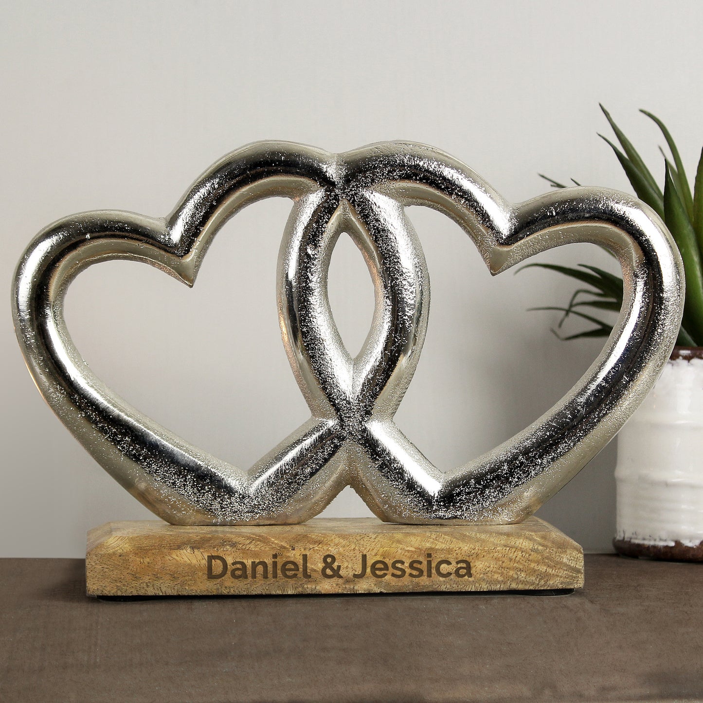 Decorative sculpture of two interlocking hearts on a wooden base with 'Daniel & Jessica' engraving, against a neutral background.