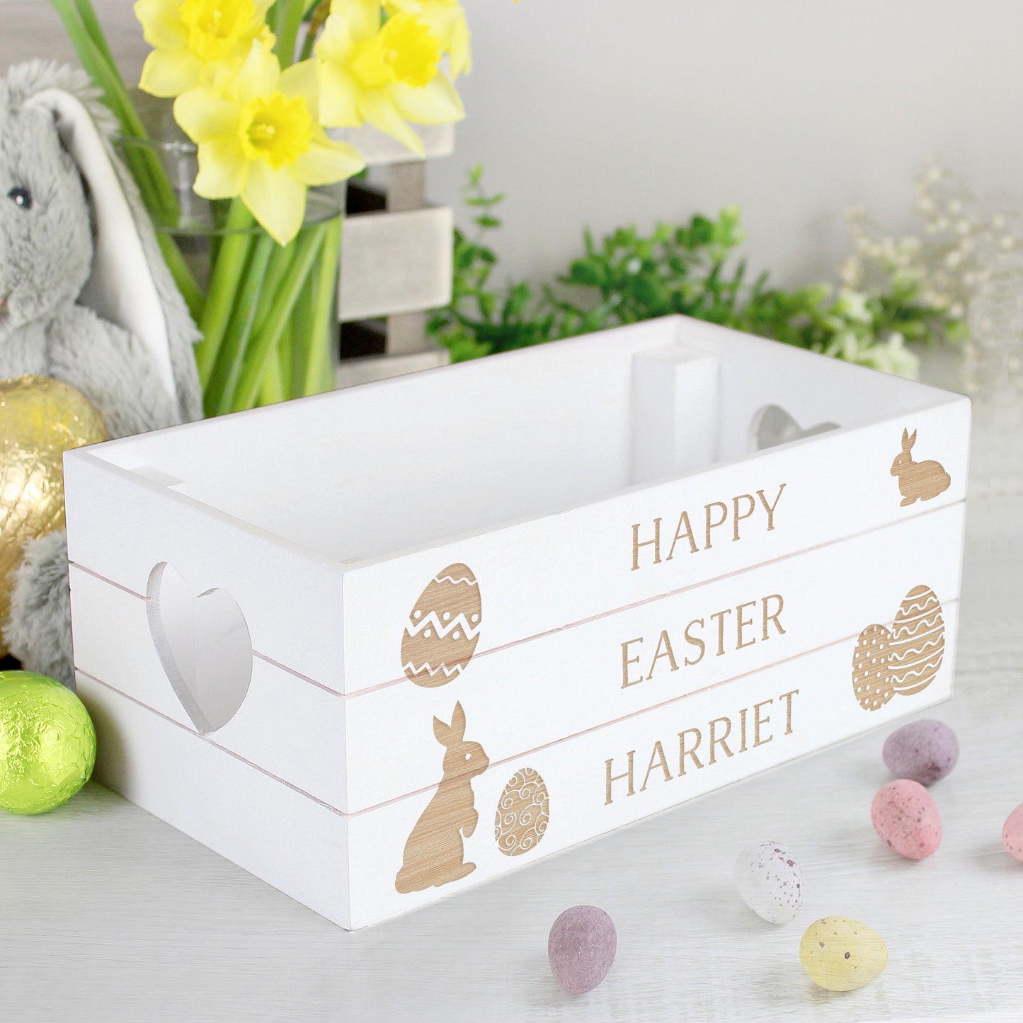 White Easter-themed wooden crate with 'Happy Easter Harriet' text, surrounded by decorative items on a light surface.