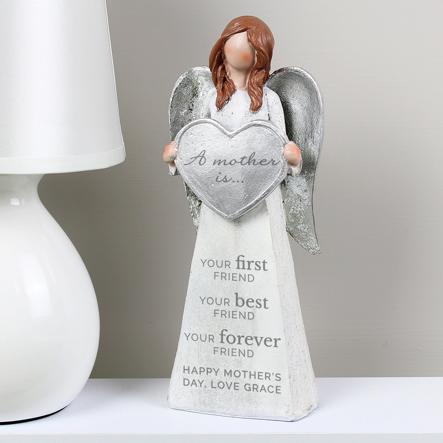 Decorative angel figurine holding a heart-shaped plaque with text on a white surface.