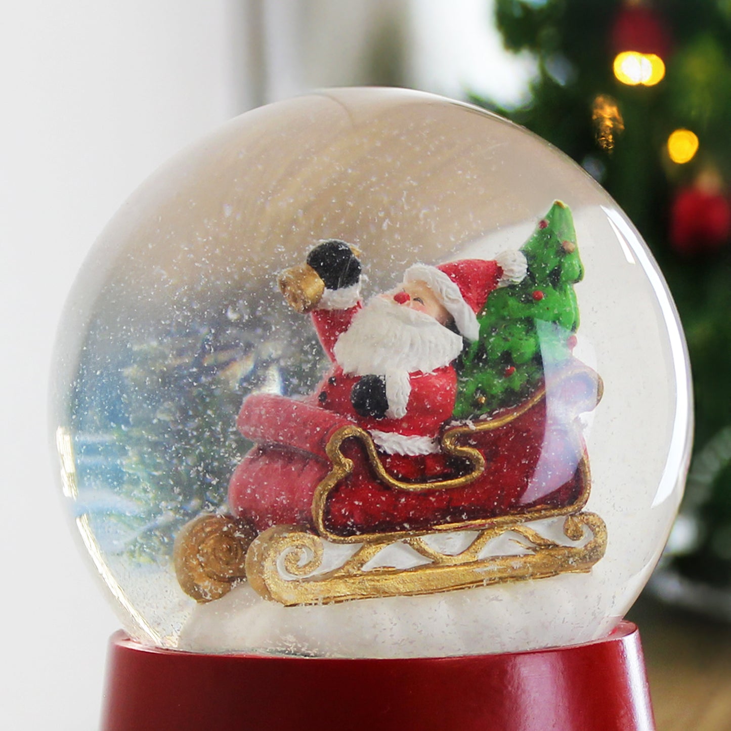 Snow globe with Santa Claus on a sleigh inside, against a blurred Christmas tree background.