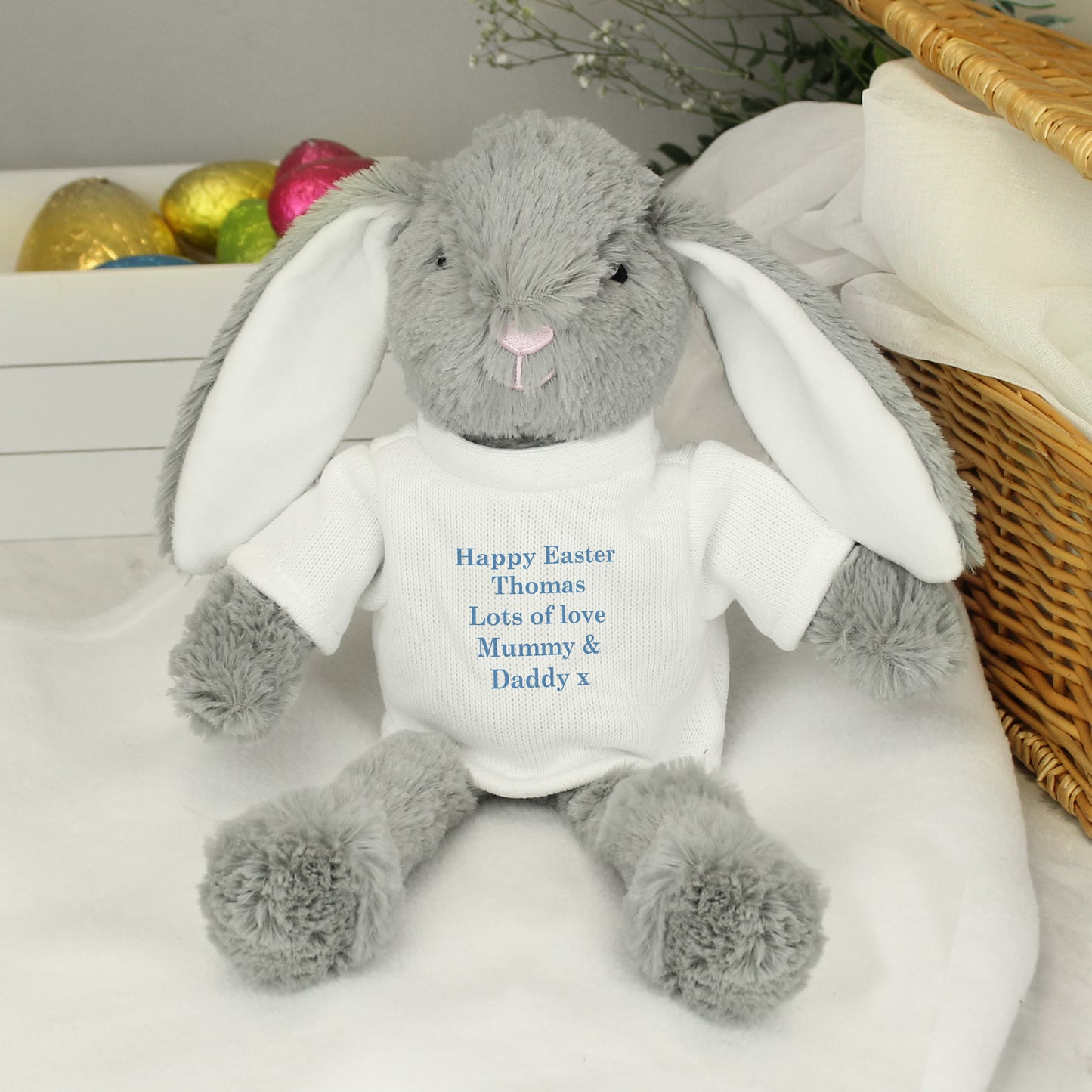 Grey plush bunny with a white shirt displaying personalised text, sitting on a white surface.
