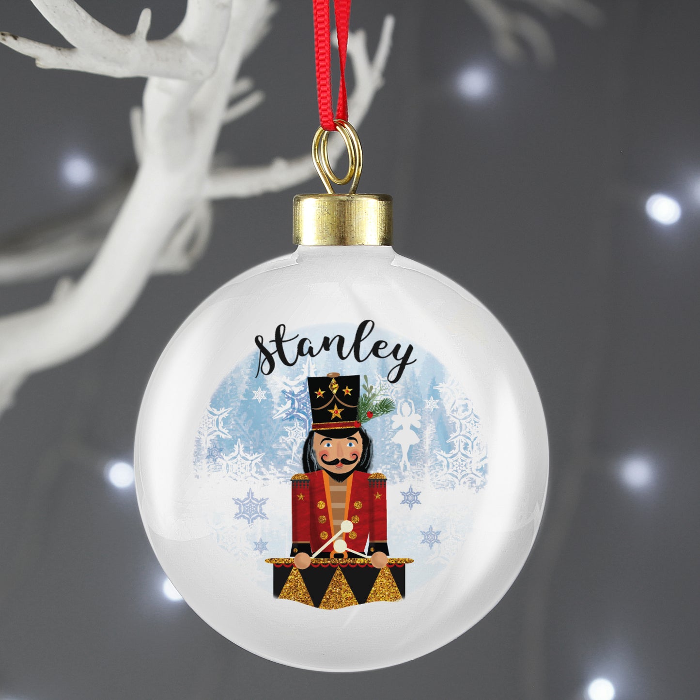 White Christmas bauble with a red ribbon, personalised with the name Stanley and a drum-playing nutcracker in a red and black uniform