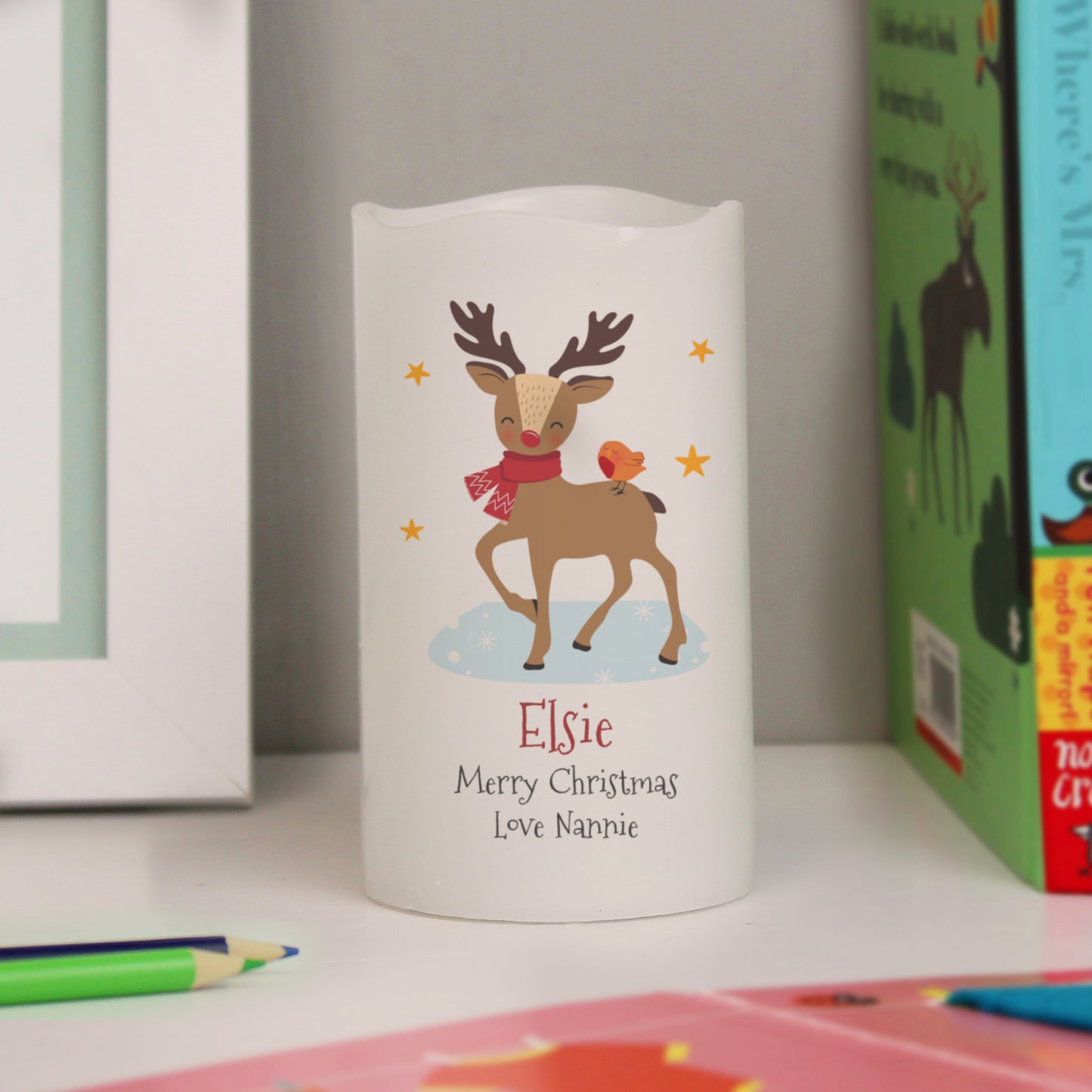 White LED candle with reindeer design and text on a surface with books and stationery.