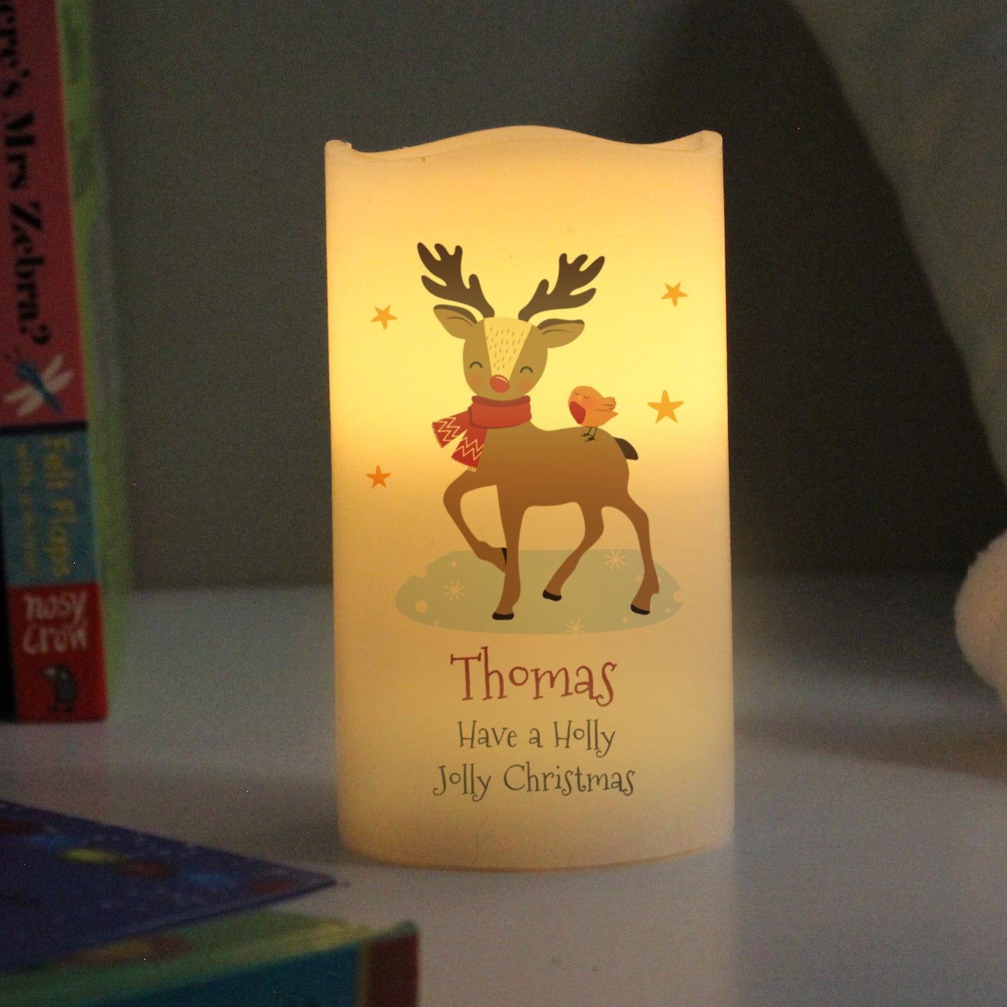 Candle with reindeer design and 'Thomas Have a Holly Jolly Christmas' text on a dark background.