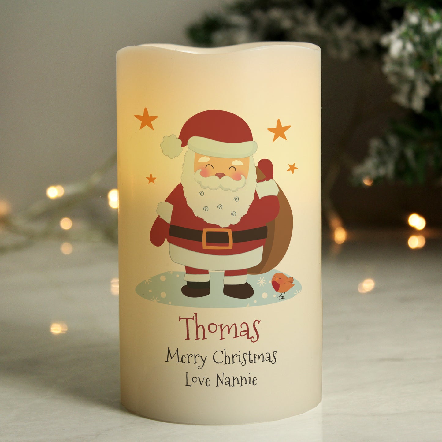 Decorative candle with Santa Claus illustration and personalised text, set against a blurred festive background.