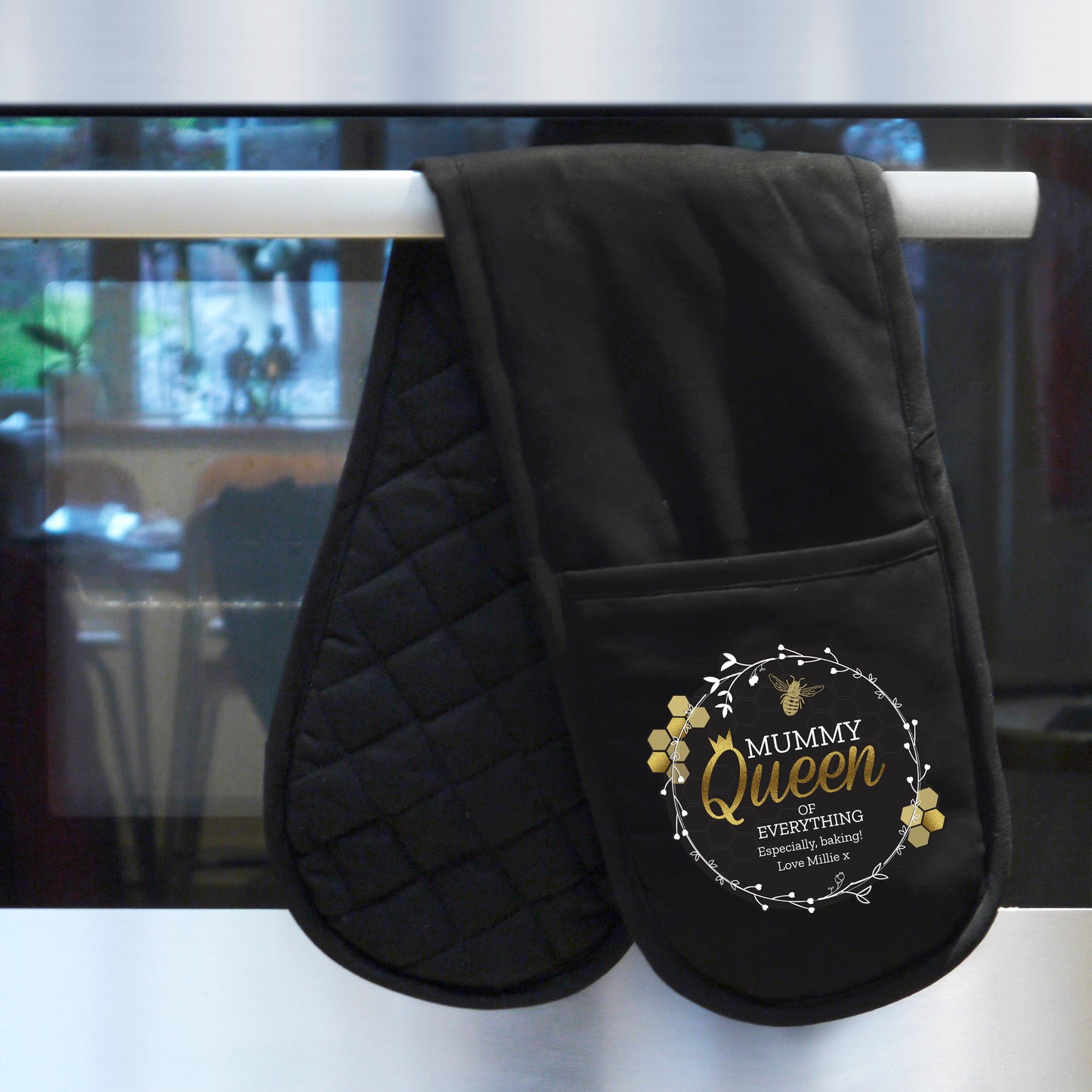 Black oven mitt with 'Mummy Queen of Everything' text hanging on a stove handle.