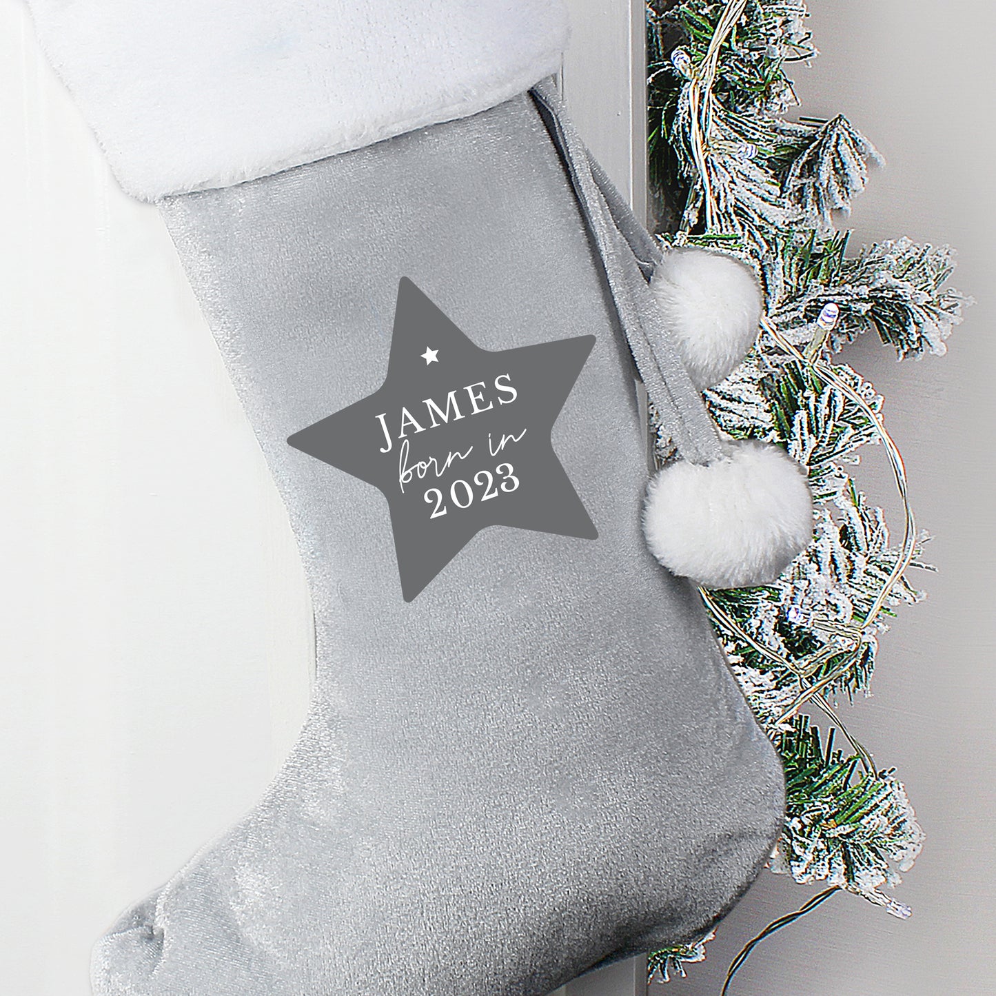 Gray Christmas stocking with a star-shaped name tag and decorative greenery.