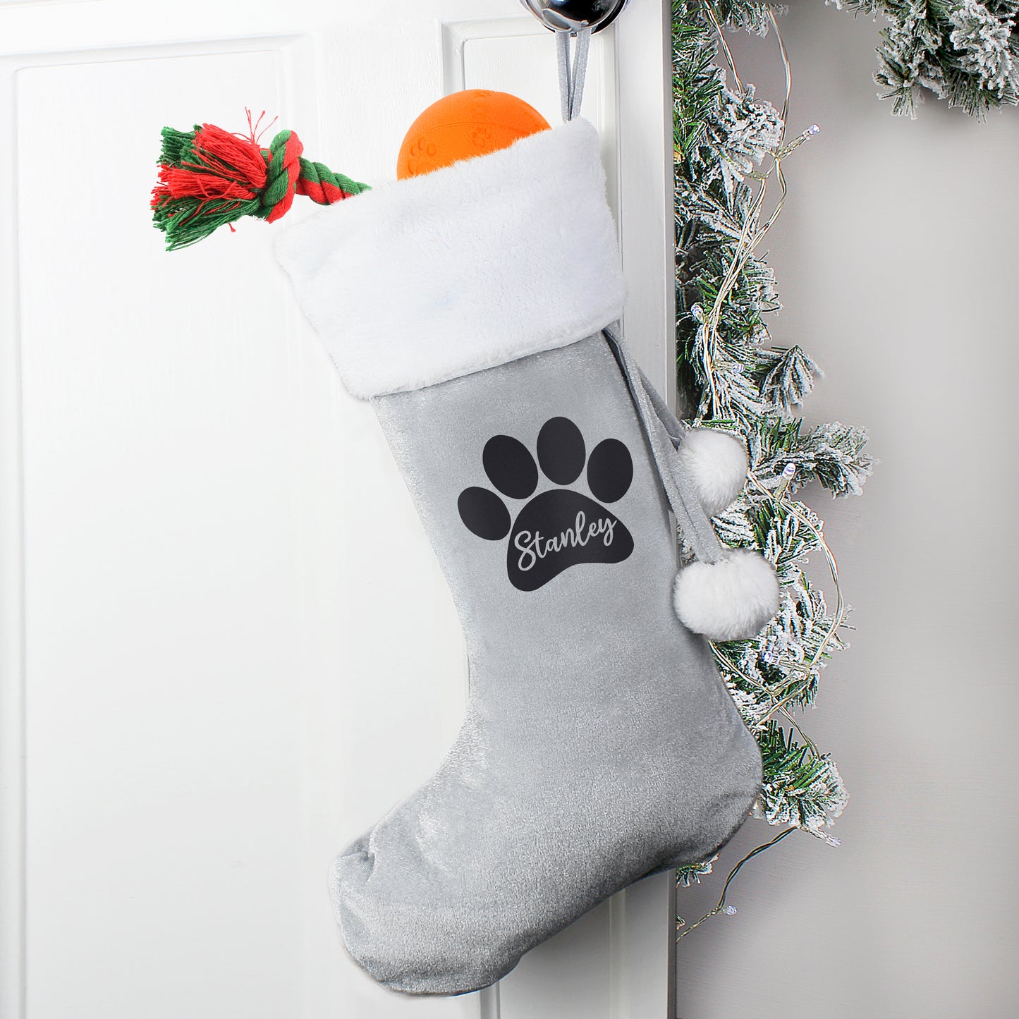 Gray Christmas stocking with a paw print and 'Stanley' text, hanging on a white door with festive decorations.