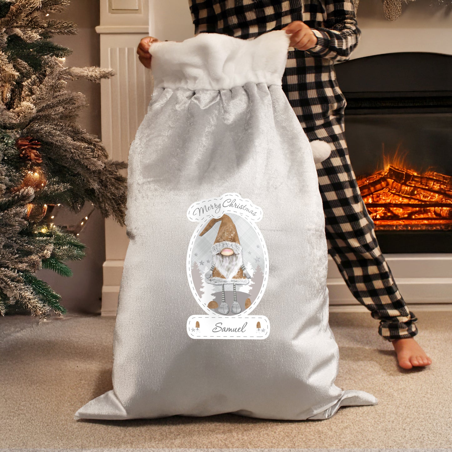 Person holding a grey Christmas sack with a personalised design in front of a fireplace.