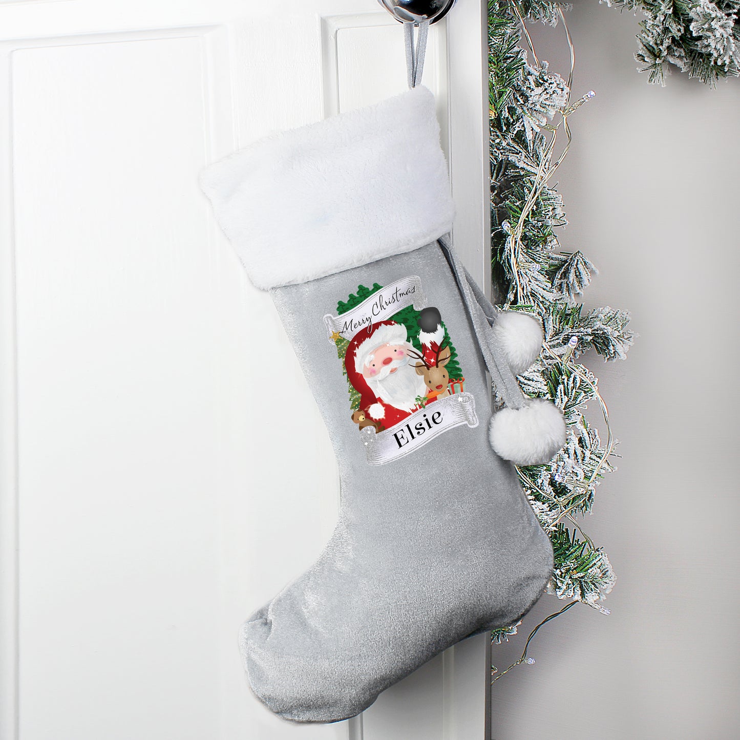 Grey Christmas stocking with Santa Claus design and pom-poms, hanging on a white door with greenery.